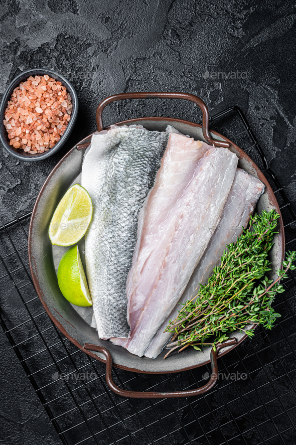 Raw Sea Bass fillet, Labrax fish with herbs and lime. Black background