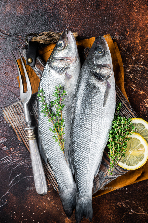 Raw Sea Bass, Branzino fish with thyme and lemon. Dark background. Top