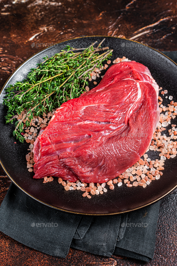 Raw beef sirloin steak with herbs and salt. Dark background. Top view