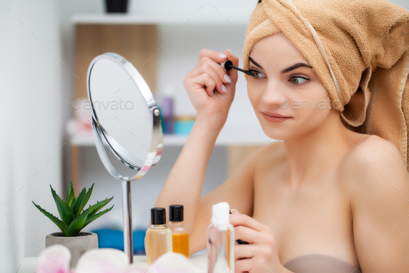 Pretty young woman puts makeup on the face in the bathroom.