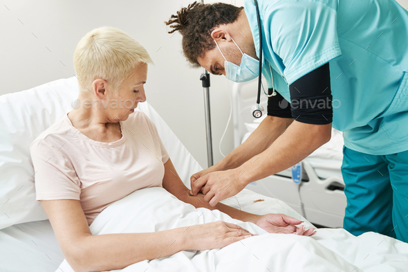 Medical person inserting needle of IV line into lady arm