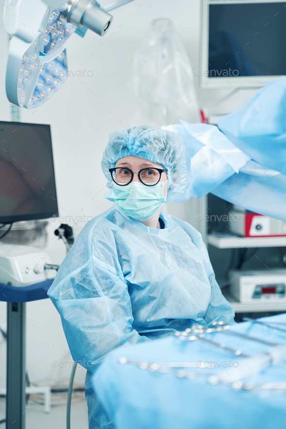 Circulating nurse near instrument table staring at camera - Stock Photo - Images