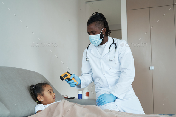 Adult man in a medical suit measures the temperature of a child