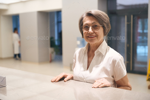 Elderly woman stands at the reception desk in spacious lobby