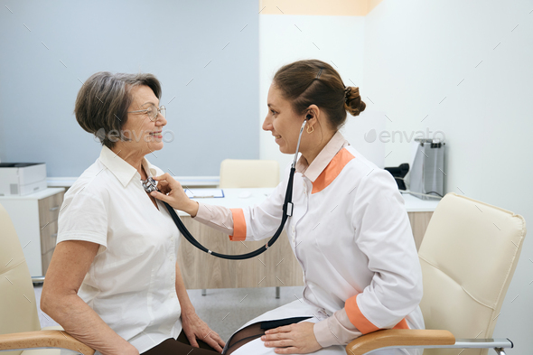 Female therapist listens to the chest of an elderly patient - Stock Photo - Images