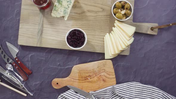 Flat lay. Arranging gourmet cheese, crakers, and fruits on a board for a large cheese board. alt