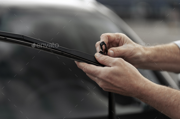 Details on technician\'s hands changing windshield wipers blades on car. Installation of car wipers
