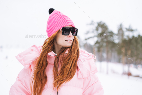 Young red haired woman in pink sportswear and sunglasses on winter snowy background - Stock Photo - Images