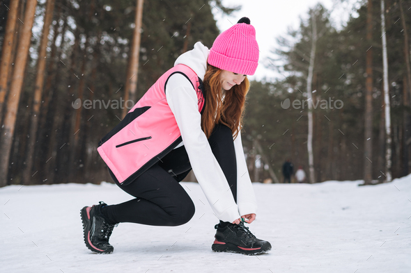 Young red haired woman in pink sportswear running in winter snowy forest - Stock Photo - Images