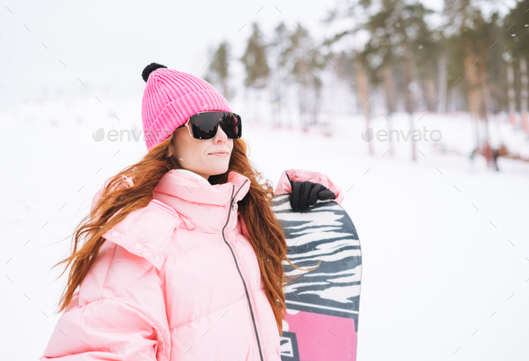 Young red haired woman in pink sportswear with snowboard on winter snowy background - Stock Photo - Images