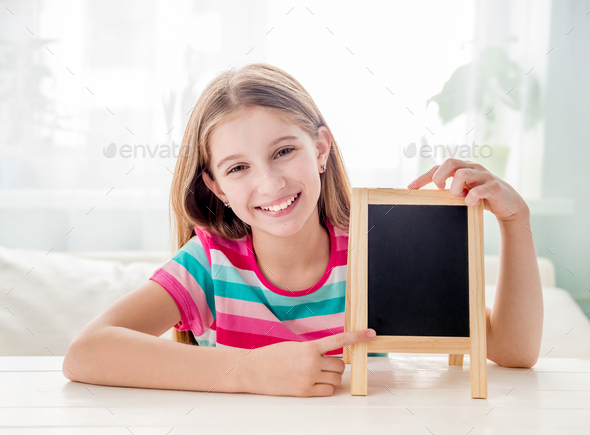 Smiling little girl sitting at a table with empty small chalkboard