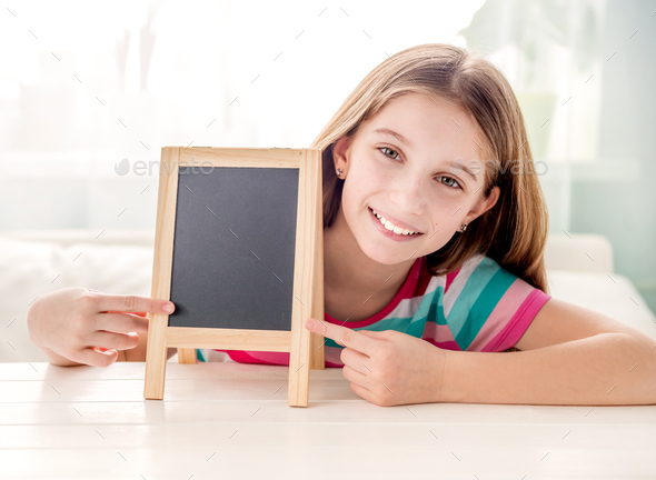 Smiling little girl sitting at a table with empty small chalkboard