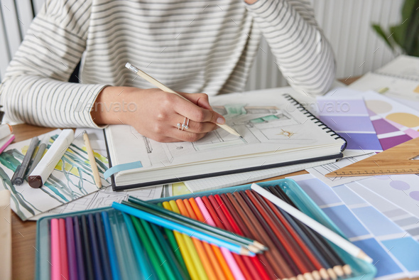 Cropped shot of unknown creative woman draws picture in album engaged in favorite activity develops