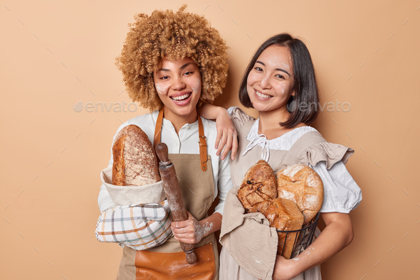 Horizontal shot of happy female bakers work together as team pose with loaves of freshly baked bread