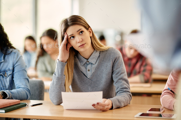 Female student feeling worried before writing an exam at university classroom.