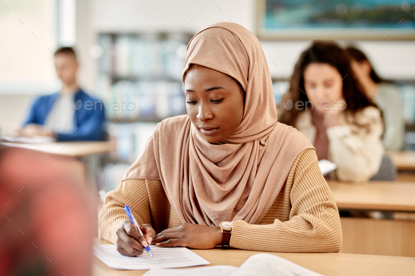 Black Muslim woman writing an exam in the classroom at the university.