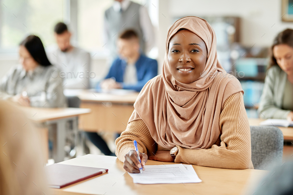 Happy black woman in hijab attending a lecture at university classroom.
