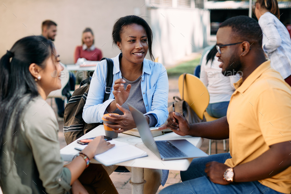 Happy black student and her friends talking on coffee break at college  cafeteria. Stock Photo by drazenphoto