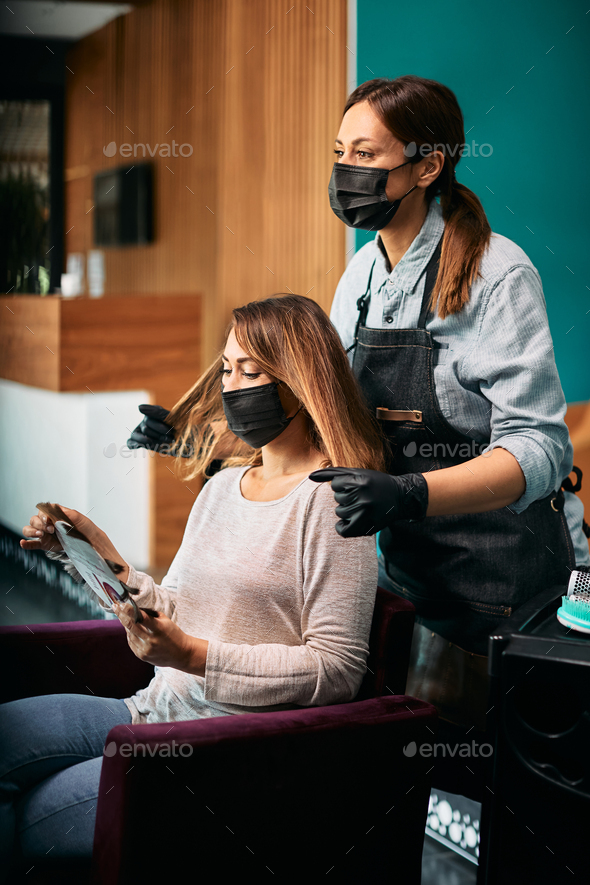 Hairdresser and her female client wearing protective face masks during appointment at hair salon.
