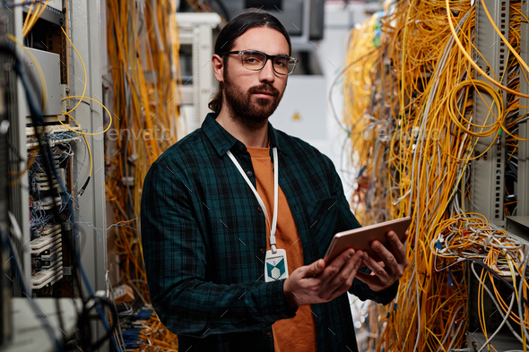 System administrator standing in server room and looking at camera - Stock Photo - Images
