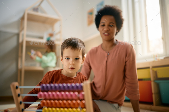 Small boy learning to count on abacus with his preschool teacher.