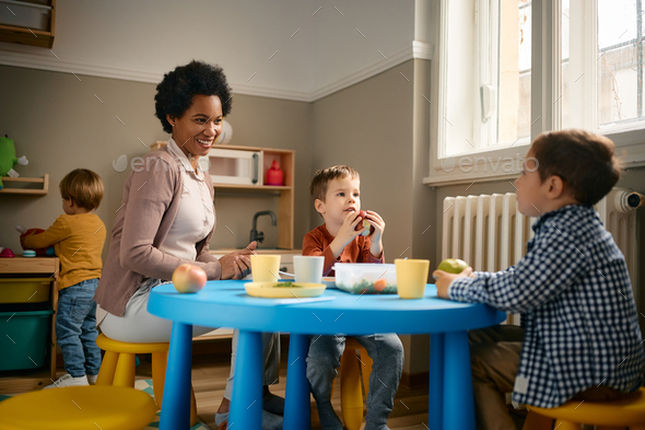 Happy black teacher and small boys enjoying during lunch break at kindergarten. - Stock Photo - Images