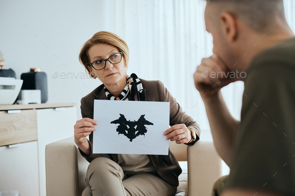 Mature psychiatrist evaluating mental disorder of soldier with inkblot test during counseling.