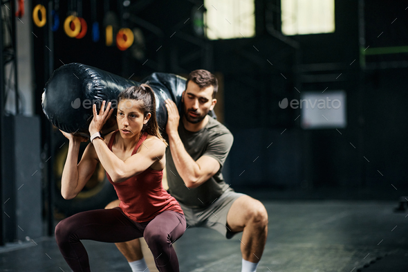 Black sporty young man working out with sandbag while exercises in
