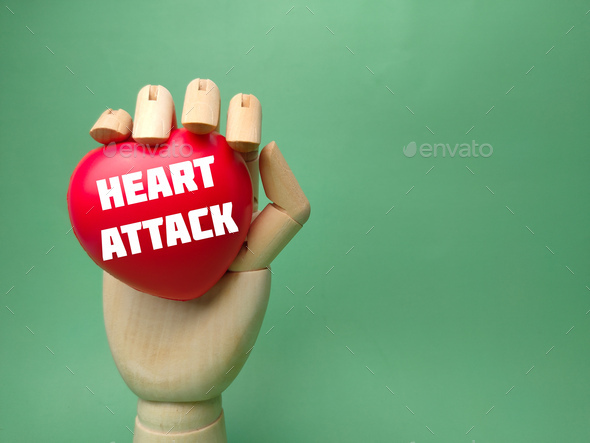 Wooden hand holding red heart with the word HEART ATTACK on a green background. - Stock Photo - Images