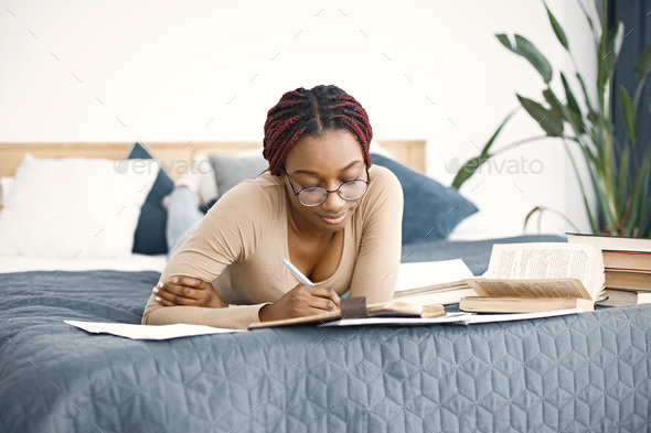 Young teenage girl lying on her bed studying in light bedroom at home - Stock Photo - Images