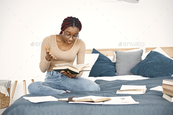 Young teenage girl sitting on her bed studying in light bedroom at home - Stock Photo - Images