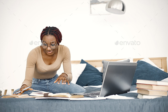 Young teenage girl sitting on her bed studying and using a laptop - Stock Photo - Images