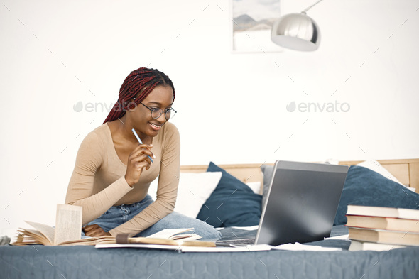 Young teenage girl sitting on her bed studying and using a laptop - Stock Photo - Images