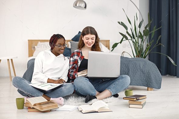 Two young teenage girls sitting on a floor near bed studying and using a laptop - Stock Photo - Images