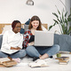 Two young teenage girls sitting on a floor near bed studying and using a laptop - PhotoDune Item for Sale