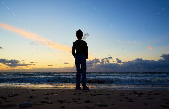 Child silhouette standing on sea beach and looking on waves - Stock Photo - Images