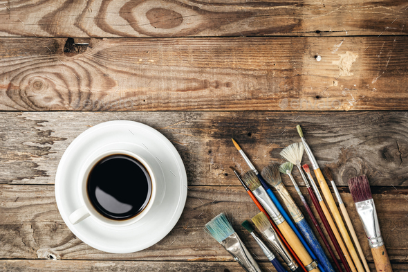 Paint brushes and a cup of coffee on a wooden background, flat lay. - Stock Photo - Images