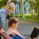 cute caucasian boys sitting on bench in park with laptop computer. Black screen - PhotoDune Item for Sale