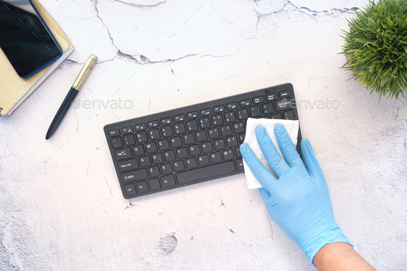 hand in blue rubber gloves and white tissue disinfecting keyboard