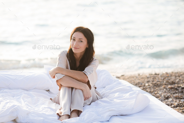 Smiling woman wear pajama in bed resting over sea background outdoor - Stock Photo - Images