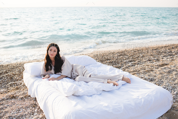 Smiling woman wear pajama in bed resting over sea background outdoor - Stock Photo - Images