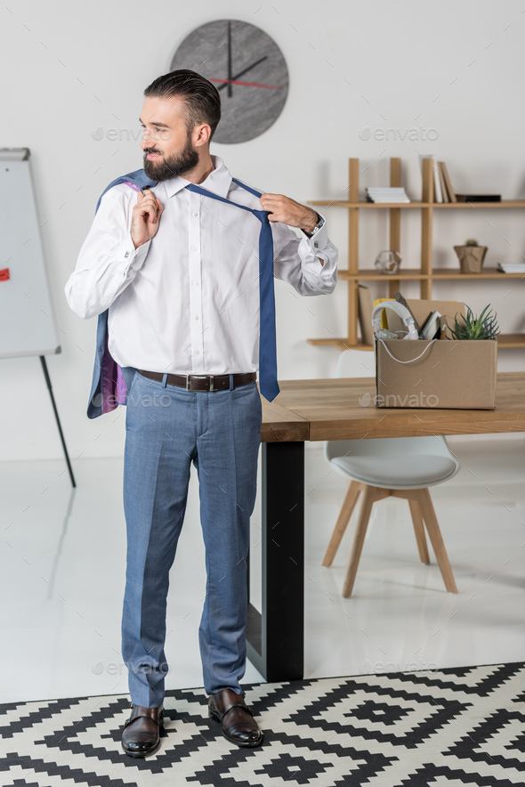 smiling businessman with jacket in hand untying tie in office, quitting job concept