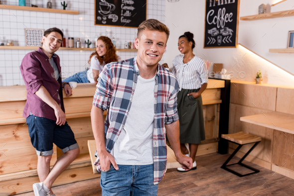 handsome young cheerful man smiling at camera while happy friends standing behind in cafe - Stock Photo - Images