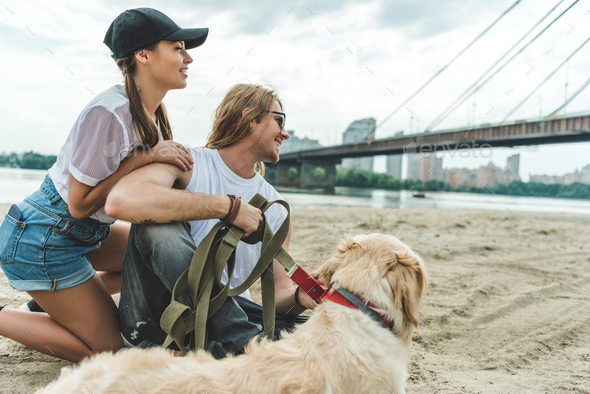 beautiful young couple with dog on beach looking away - Stock Photo - Images