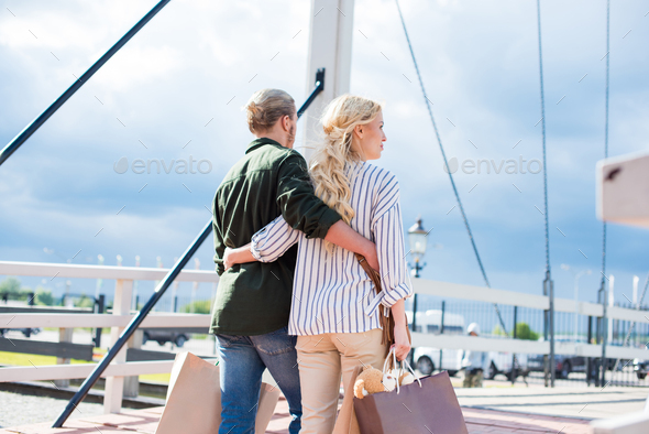 rear view of casual couple holding shopping bags while walking together on the bridge - Stock Photo - Images