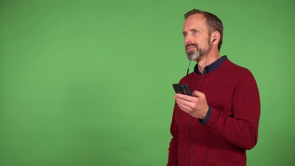 A Middleaged Man Listens to Music with Earphones on and a Smartphone with a Smile  Green Screen