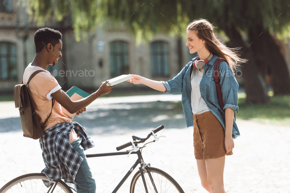 african american student with bicycle and female student with books near college - Stock Photo - Images