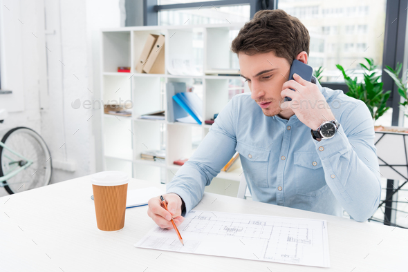 male architect working with blueprint and using smartphone in modern office - Stock Photo - Images