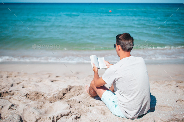 Young man sitting on the beach reading book - Stock Photo - Images