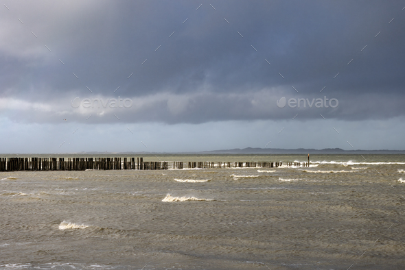 North Sea with wooden poles in a cloudy and windy day at Breskens - Stock Photo - Images